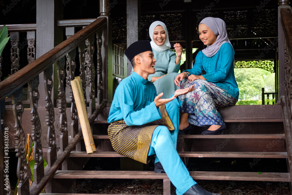 A group of malay muslim people in traditional costume having happy conversation during Aidilfitri celebration at terrace of traditional wooden house