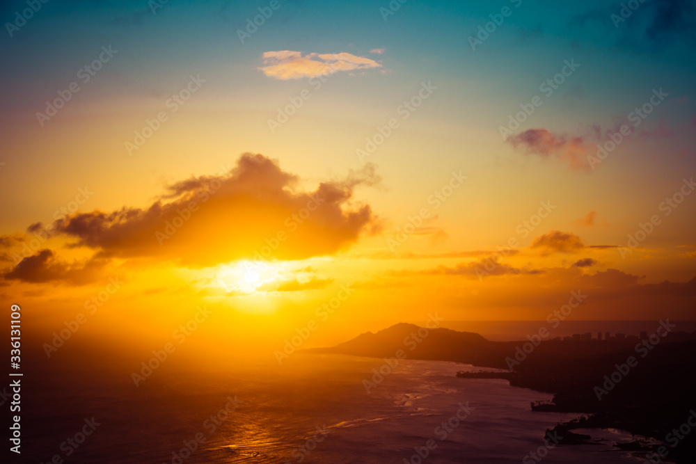 A sunset over the Hawaiian Island of Oahu as seen from a mountain top with the city of Waikiki Beach and Diamond Head in the distance.  Image captured from the summit of Koko Head Crater.