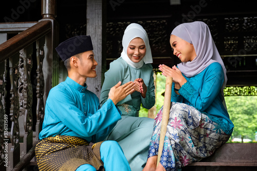 A group of malay muslim people in traditional costume showing greeting gesture during Aidilfitri celebration at terrace of traditional wooden house