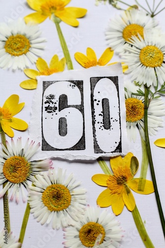 Sixtieth  birthday card image, a stamped number sixty surrounded by pressed flowers, daisies and yellow lesser celandine wildflowers . A nature inspired, fresh background.  