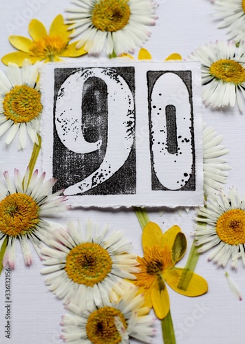 Ninetieth  birthday card image, a stamped number ninety  surrounded by pressed flowers, daisies and yellow lesser celandine wildflowers . A nature inspired, fresh background.  