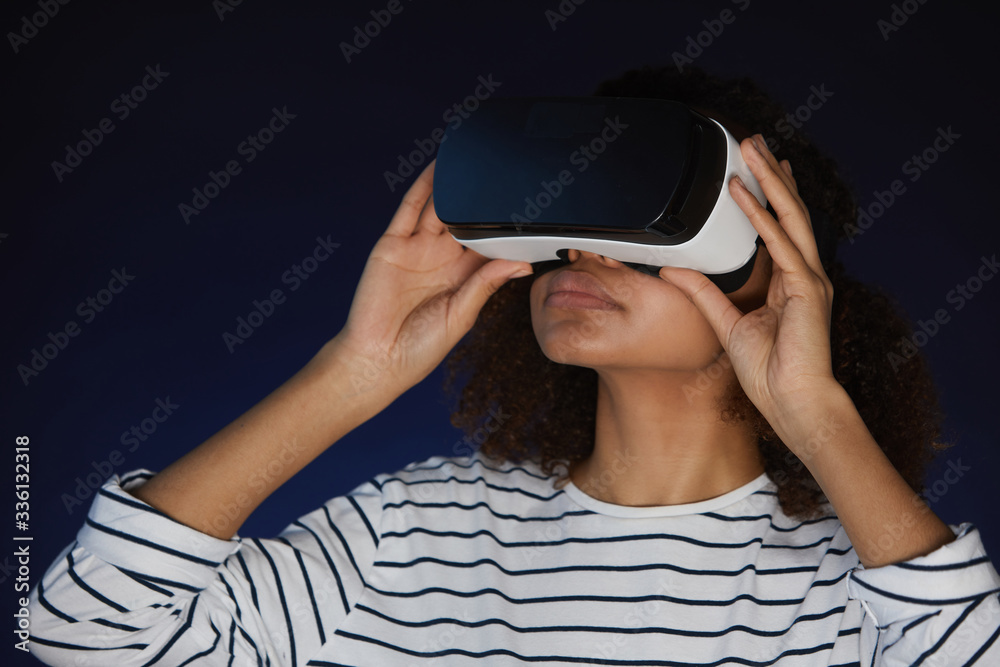 Head and shoulders portrait of mixed-race young woman wearing virtual reality gear while enjoying immersive videogame or movie in dark Head and shoulders portrait of mixed-race young woman wearing virtual reality gear while enjoying immersive videogame or movie in dark