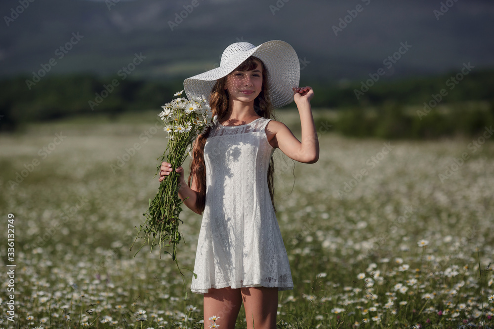 Beautiful teen girl on a walk in a daisy field in a white dress