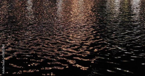 Pond water surface at night with steet lamps reflecting on ripples photo