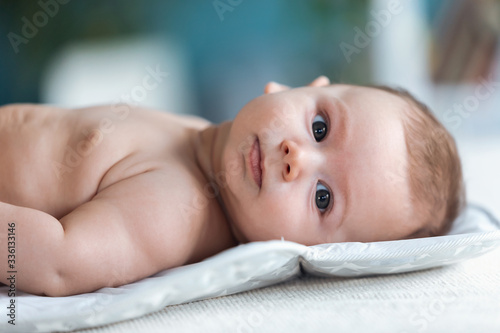 Happy baby looking at camera while lying on white sheet at home.