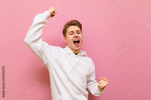 Canvas Print Closeup portrait of a smiling guy emotionally rejoices with his hands raised, smiling and looking into the camera on a pink background
