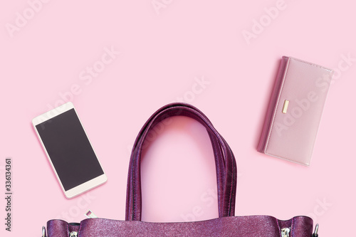 Beautiful fashionable purple bag with new smartphone  and leather wallet on  delicate pink background.