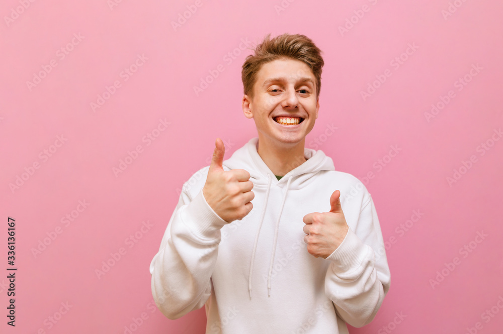 Cheerful young blond man looking into the camera and showing thumbs up with a smile on his face isolated on pink background. Positive guy shows gesture like and rejoices. Copy space Cheerful young blond man looking into the camera and showing thumbs up with a smile on his face isolated on pink background. Positive guy shows gesture like and rejoices. Copy space