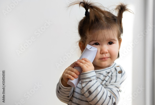 Sweet baby girl holding electronic thermometer and check out temperature. photo