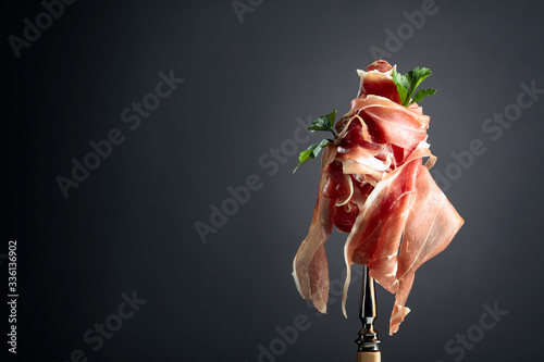 Thin sliced prosciutto with parsley on a fork. Traditional Italian cuisine.