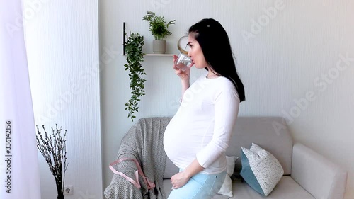Pregnant woman drinking water. Healthy lifestyle. Expecting woman indoor. Pregnancy dehydration avoidance. female holding a glass of water. photo