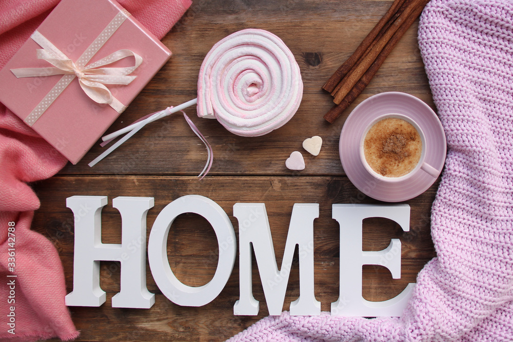 cappuccino with cinnamon in a pink cup, a gift in a box, sweets, candles, cones, plaid on an old wooden table, the word home, top view, flat, concept cozy home, copy space