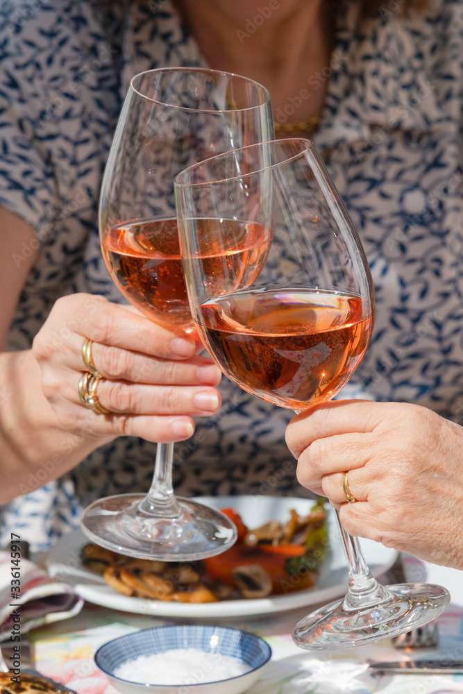 hands of two woman toasting with glasses of rose wine.