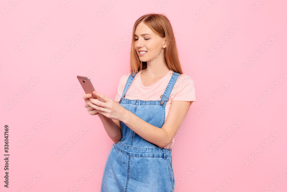 Attractive young woman writing a message on a smartphone on an isolated pink background Attractive young woman writing a message on a smartphone on an isolated pink background