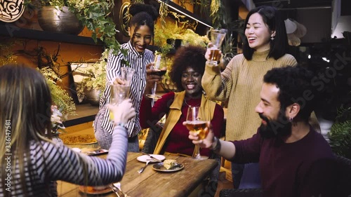  A group of friends from various ethnic groups enjoy happily and toast in a restaurant and bar with a very careful and elegant decoration
