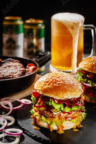 A big hamburger with a glass of beer on a table. Fast food. Junk food. Close up
