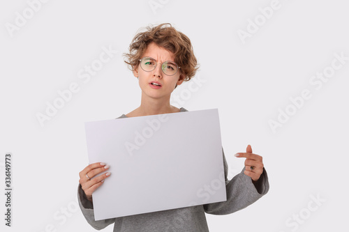 Concerned young woman with eyeglass holding empty blank paper board with copy space