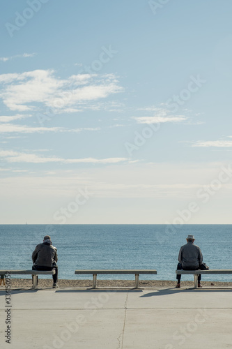Bare man and man with hat sitting watching the sea at sunrise
