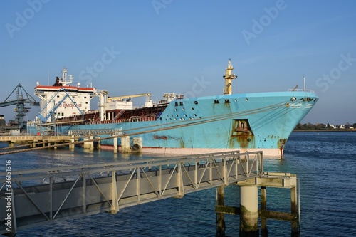 Oil Tanker ship in operation at the Petroleum products terminal of Lorient, France, with blue hull and black funnel on a sunny day. Horizontal front view.