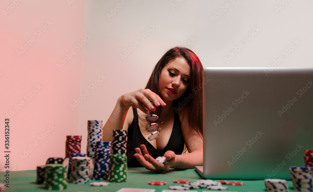 Cute girl shuffling poker chips from hand to hand while sitting in front of laptop, online poker Cute girl shuffling poker chips from hand to hand while sitting in front of laptop, online poker