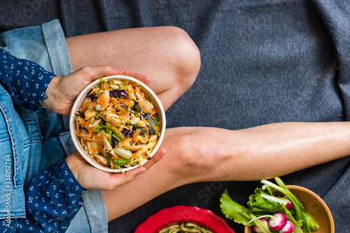 Young woman holds vegan detox dieting food with vegetables salad on legs. Top above view.