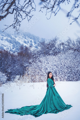 A girl in  fabulous long green dress in the snow-covered mountains. A woman in a fairy-tale dress in the mountains in winter. Winter fairytale photo session of a beautiful girl in Sairam su Kazakhstan photo