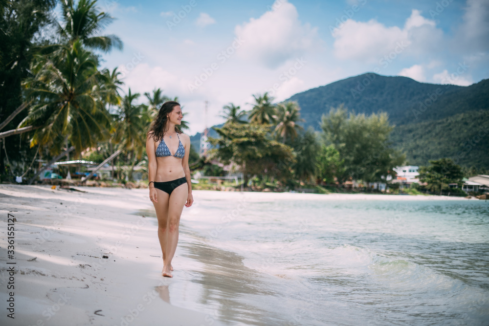 Beautiful woman in a swimsuit walks on a tropical beach