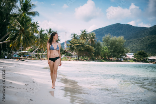 Beautiful woman in a swimsuit walks on a tropical beach © Anna