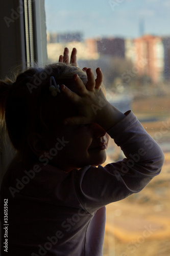 Lonely child looks out the window in quarantine conditions