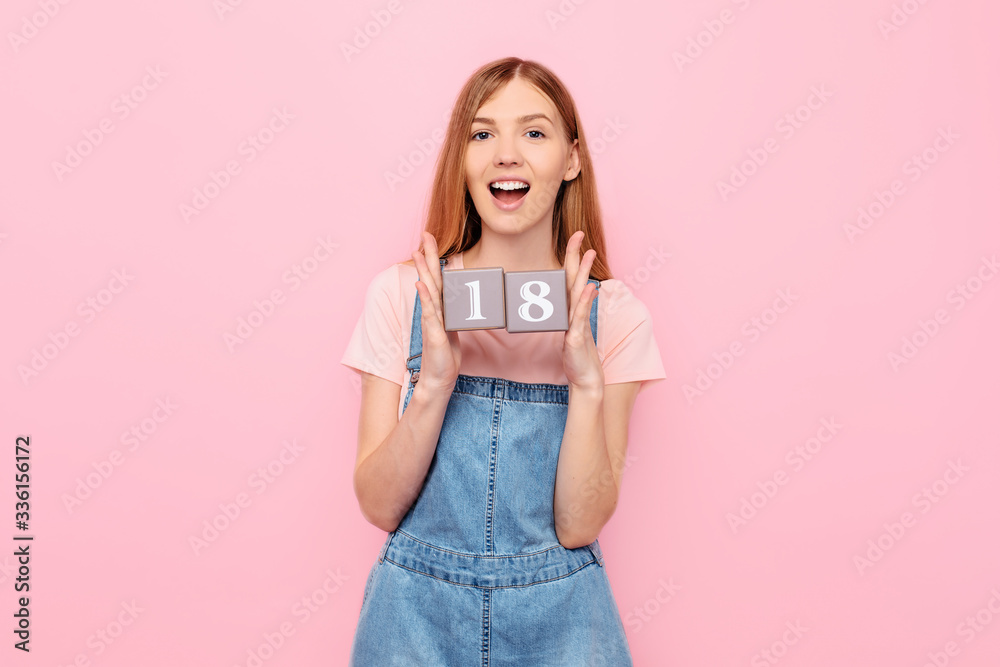 young woman is celebrating her birthday and holding cubes with her age 18 eighteen years old, on an isolated pink background young woman is celebrating her birthday and holding cubes with her age 18 eighteen years old, on an isolated pink background