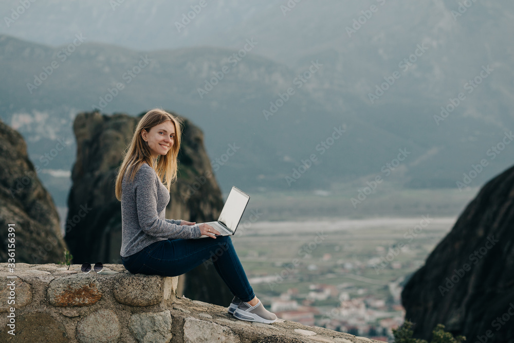 Pretty caucasian woman works remotely at high rocks at sunset