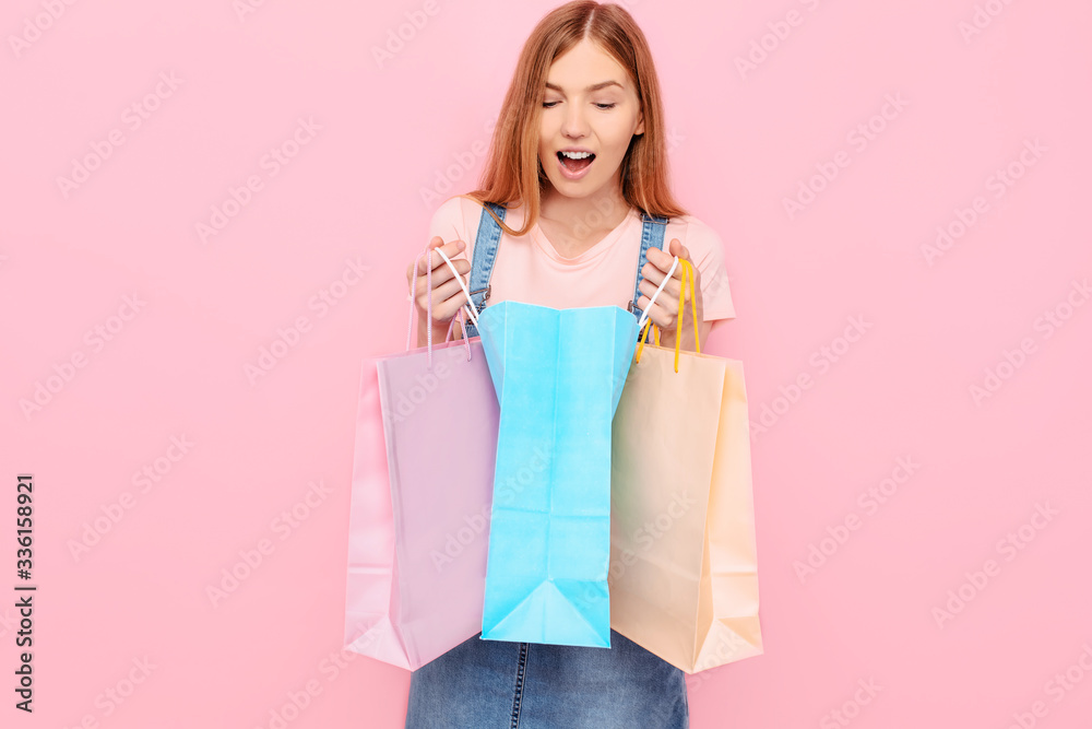 An image of a beautiful shocked surprised young stylish woman posing isolated on a pink background, holding shopping bags An image of a beautiful shocked surprised young stylish woman posing isolated on a pink background, holding shopping bags