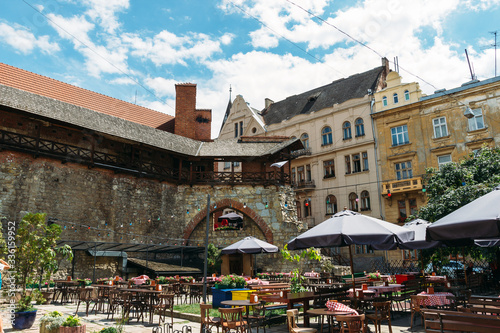 Sunny scenery of yard with stone wall and empty cafe in Ukrainian town.Coffee house at noon in Lviv. Old city street with nobody. Restaurant with tables under open sky. Summer in capital of Ukraine.