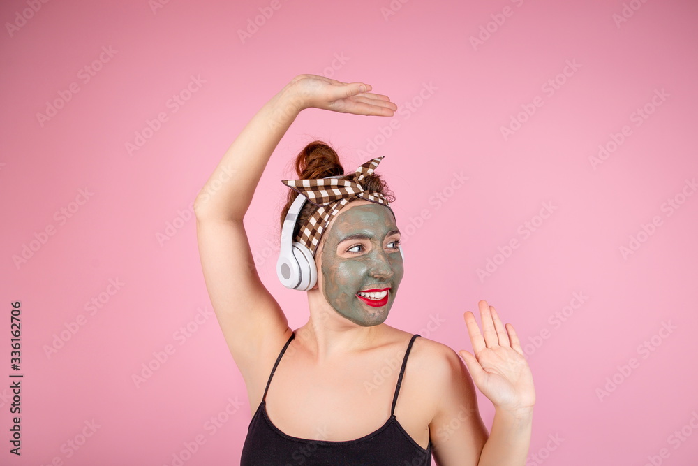 Portrait of a strange girl with red lipstick in a clay mask on her face listening to music on the earphone performing self-defense exercises Portrait of a strange girl with red lipstick in a clay mask on her face listening to music on the earphone performing self-defense exercises