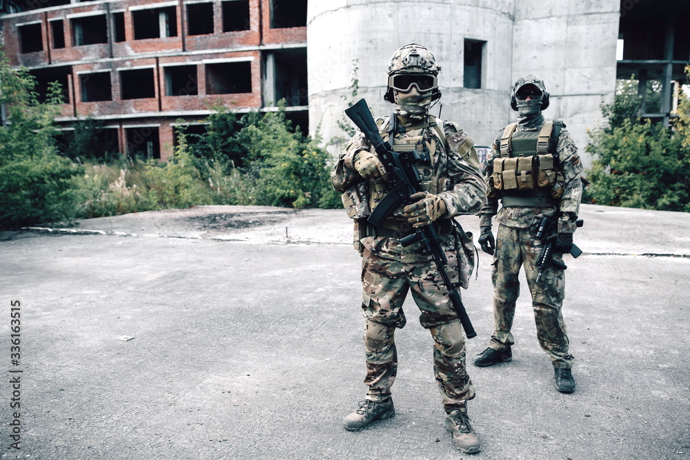 Two armed soldiers in camouflage with rifles on the background of the destroyed building patrolling the city Two armed soldiers in camouflage with rifles on the background of the destroyed building patrolling the city