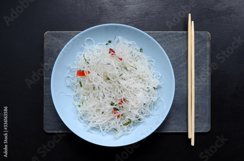 funchose glass noodles and bamboo sticks on a wooden board in blue round plate with sesame seeds on black slate background with copy space. oriental asian cuisine photo