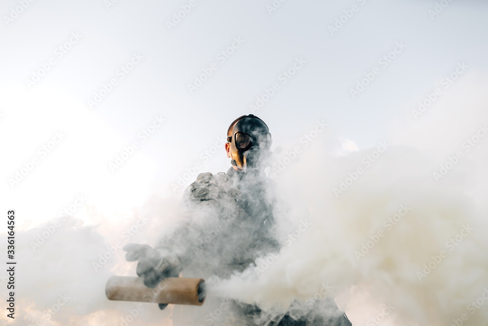 Military man in gas mask spraying a gas cylinder in front of him