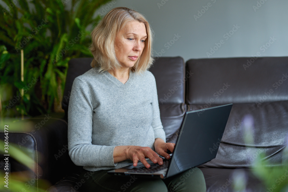 mature woman working online sitting on a sofa in an home