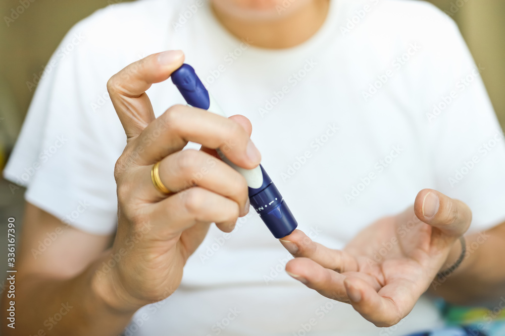 Close up of man hands using lancet on finger to check blood sugar level by Glucose meter. Use as Medicine, diabetes, glycemia, health care and people concept.