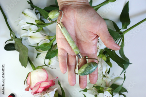 Fototapeta Naklejka Na Ścianę i Meble -  Hand holding beauty tools face roller on floral background. Face treatment. Home spa. 
