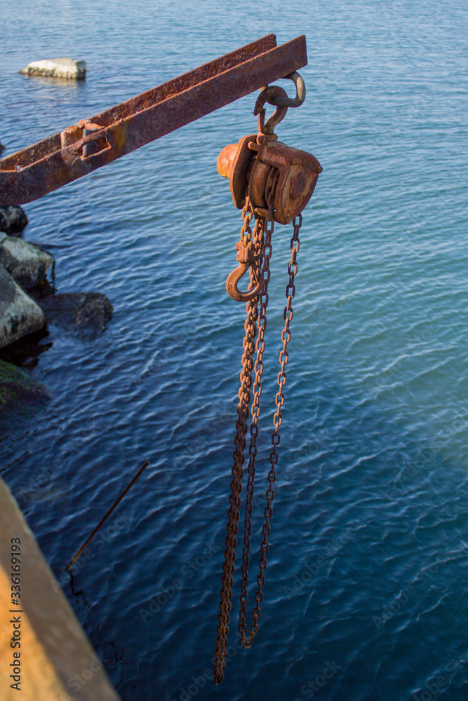 Naklejka premium rusty lever winch hanging over water on a rusty channel