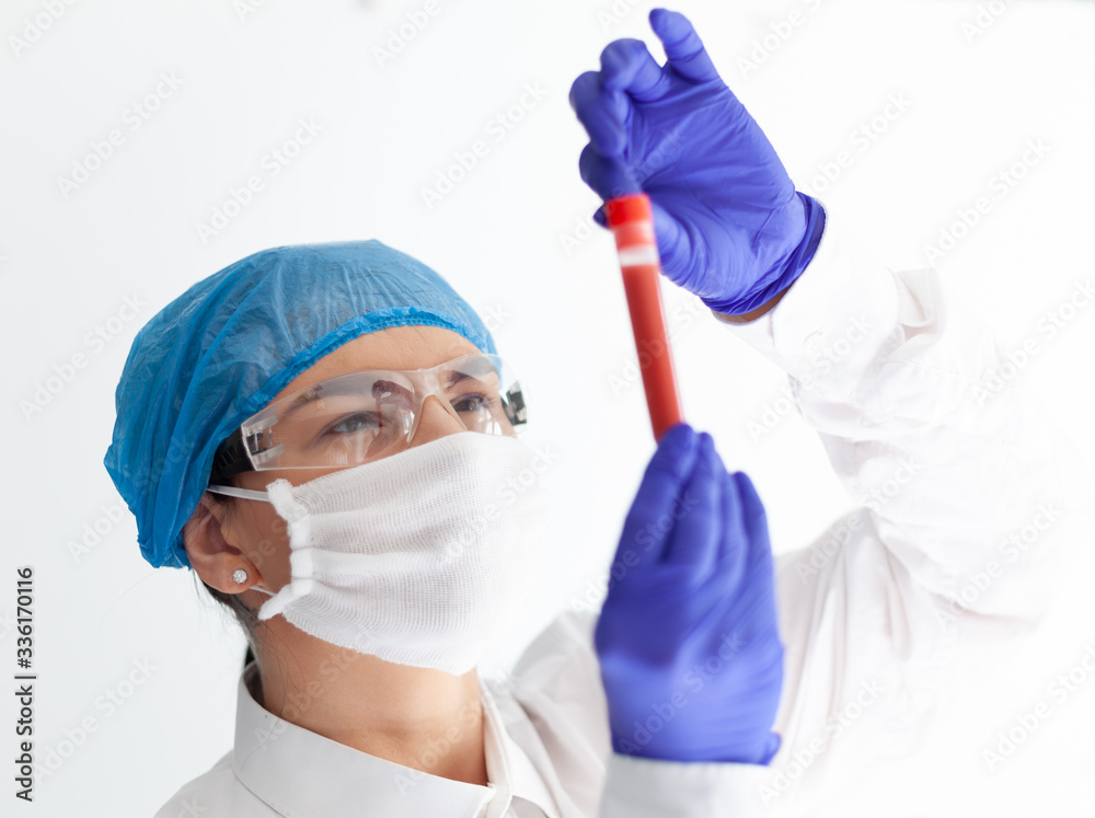 Naklejka premium female doctor in safety glasses, mask and gloves looks at a test tube with blood