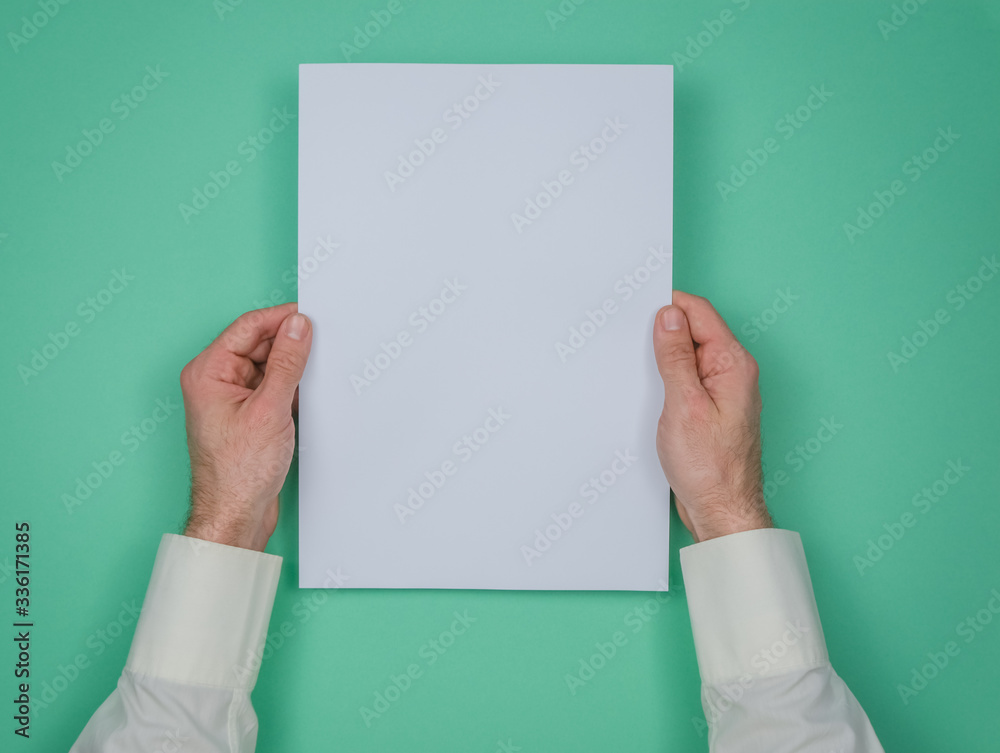 Mans hand hold a sheet of white paper on the green background. Place for a text. Mans hand hold a sheet of white paper on the green background. Place for a text.