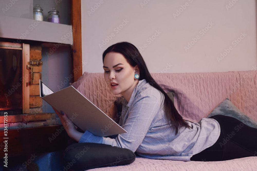 A girl sits on a sofa and studies at home. The girl looks at her notes and reads them, homework, the girl does homework at home. A girl looks in a notebook, studies, studies, university. Home school A girl sits on a sofa and studies at home. The girl looks at her notes and reads them, homework, the girl does homework at home. A girl looks in a notebook, studies, studies, university. Home school
