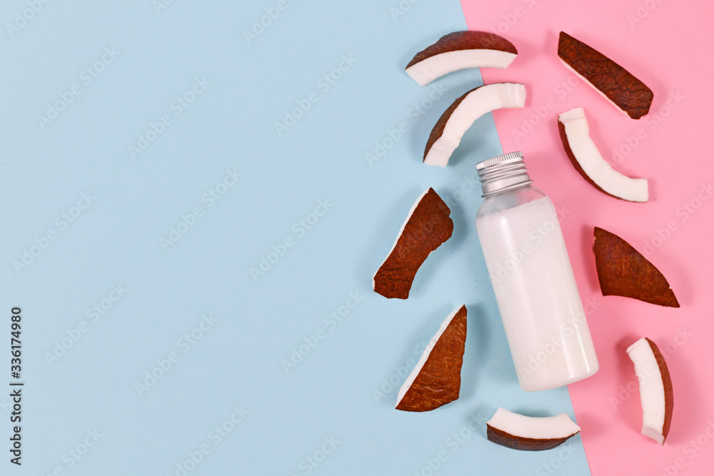 Bottle filled with coconut oil used for food preperation and cosmetic beauty products surrounded by slices of coconut fruit on blue and pink background Bottle filled with coconut oil used for food preperation and cosmetic beauty products surrounded by slices of coconut fruit on blue and pink background