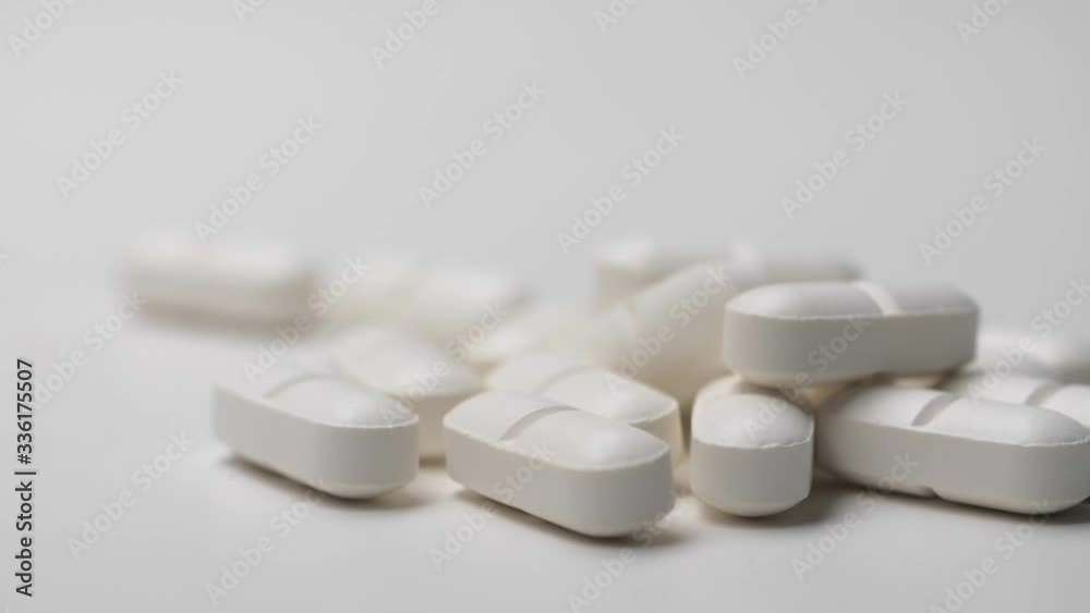 White pills sliding on white background in slow motion. White pills sliding on white background in slow motion.