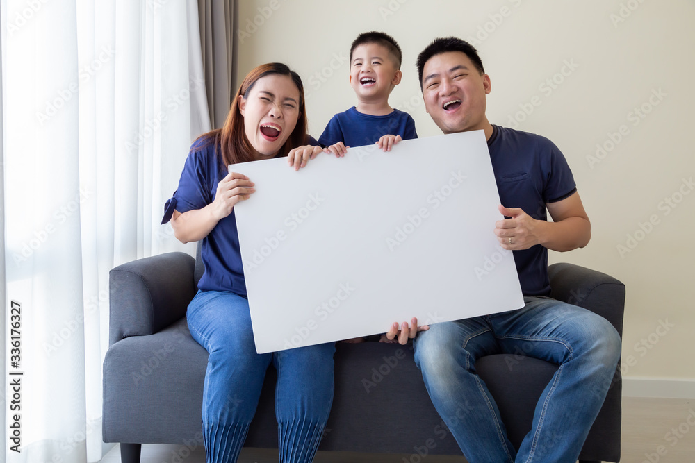 Happy Smiling Asian family holding blank big white poster and sitting on sofa in living room, Wow and surprised concept Happy Smiling Asian family holding blank big white poster and sitting on sofa in living room, Wow and surprised concept