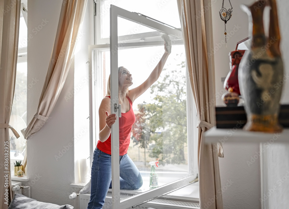 Smiling young woman cleaning window at home Smiling young woman cleaning window at home