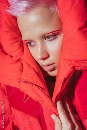 Portrait of young woman with short pink hair wearing red jacket in front of red background