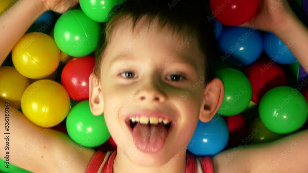 Happy cute boy jumps his head in inflatable balloons at a children's birthday party. Children's amusement park. Children's playroom in the entertainment center Happy cute boy jumps his head in inflatable balloons at a children's birthday party. Children's amusement park. Children's playroom in the entertainment center